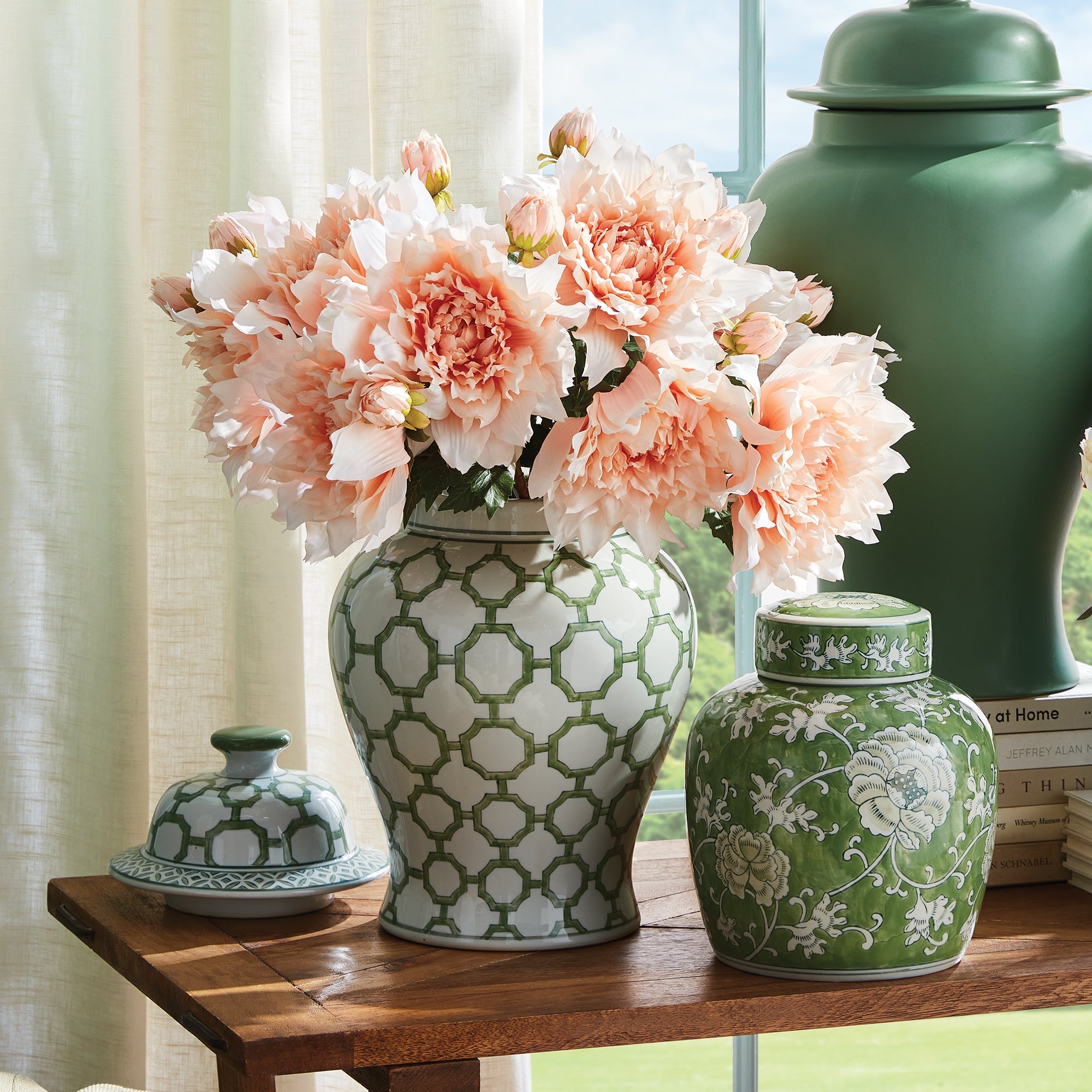 Decorative green and white vases with a bouquet of pink flowers on a wooden table.