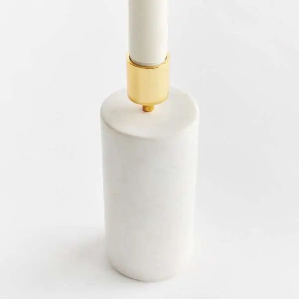 Avalyn Taper Holder, showing a modern taper candle holder with a square white marble base and a cylindrical brushed brass top. The holder is empty and is shown from a slight angle against a neutral background.