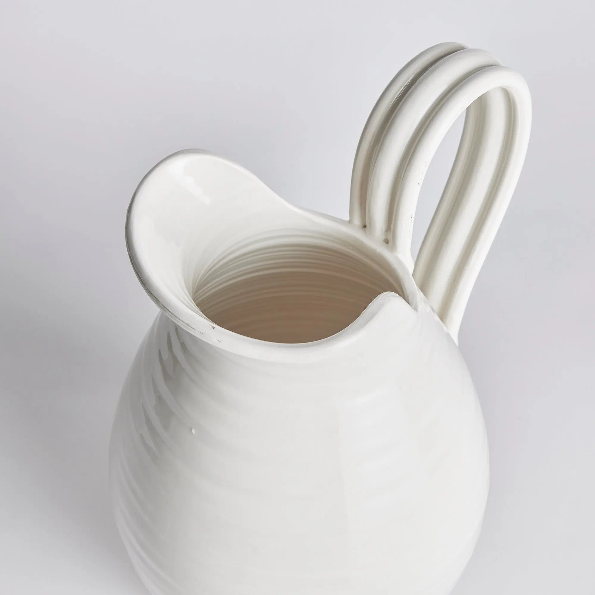 White ceramic pitcher with a handle on a light gray background