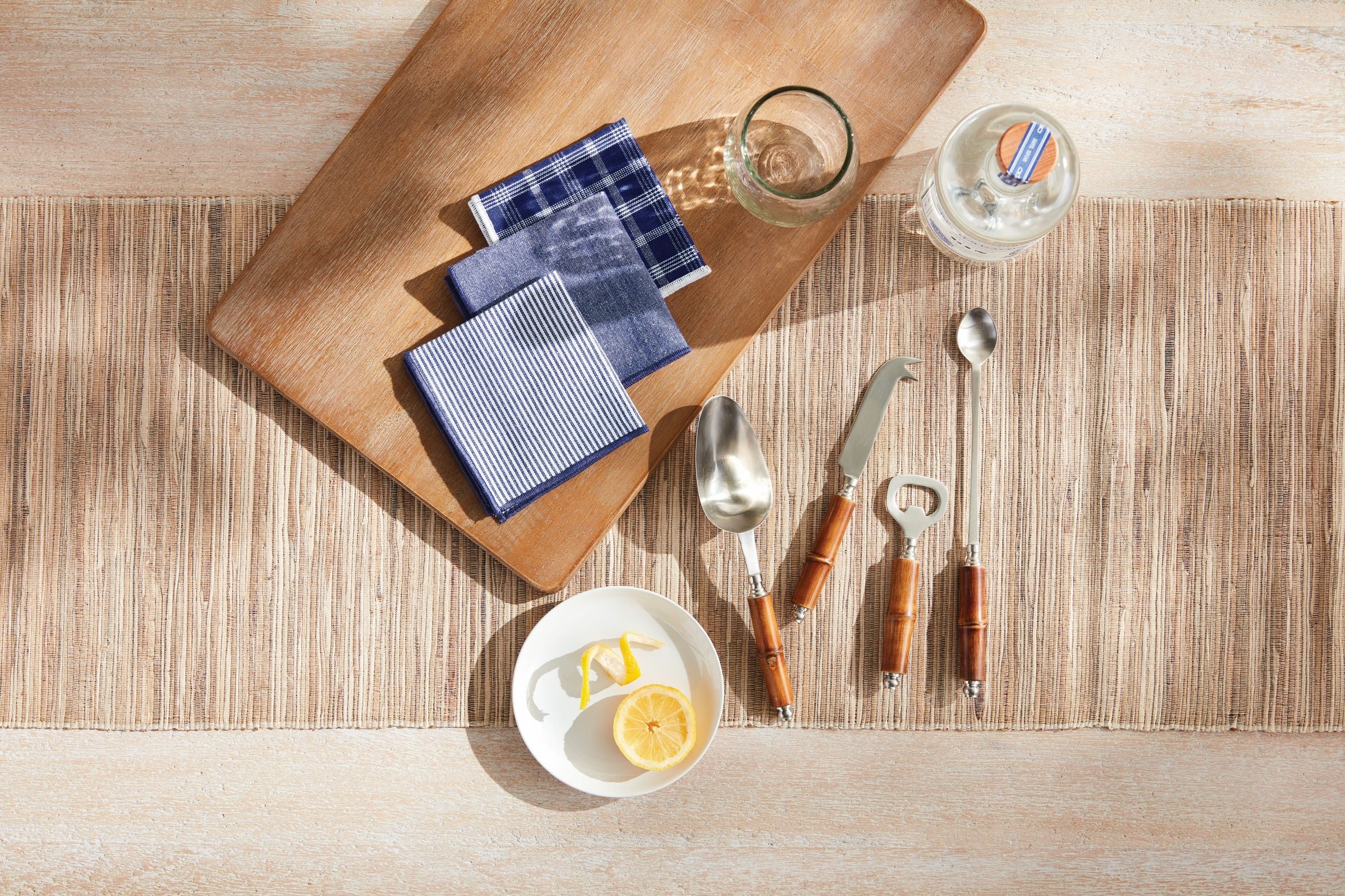 Table setting with cutting board, napkins, glasses, and cutlery on a wooden surface.