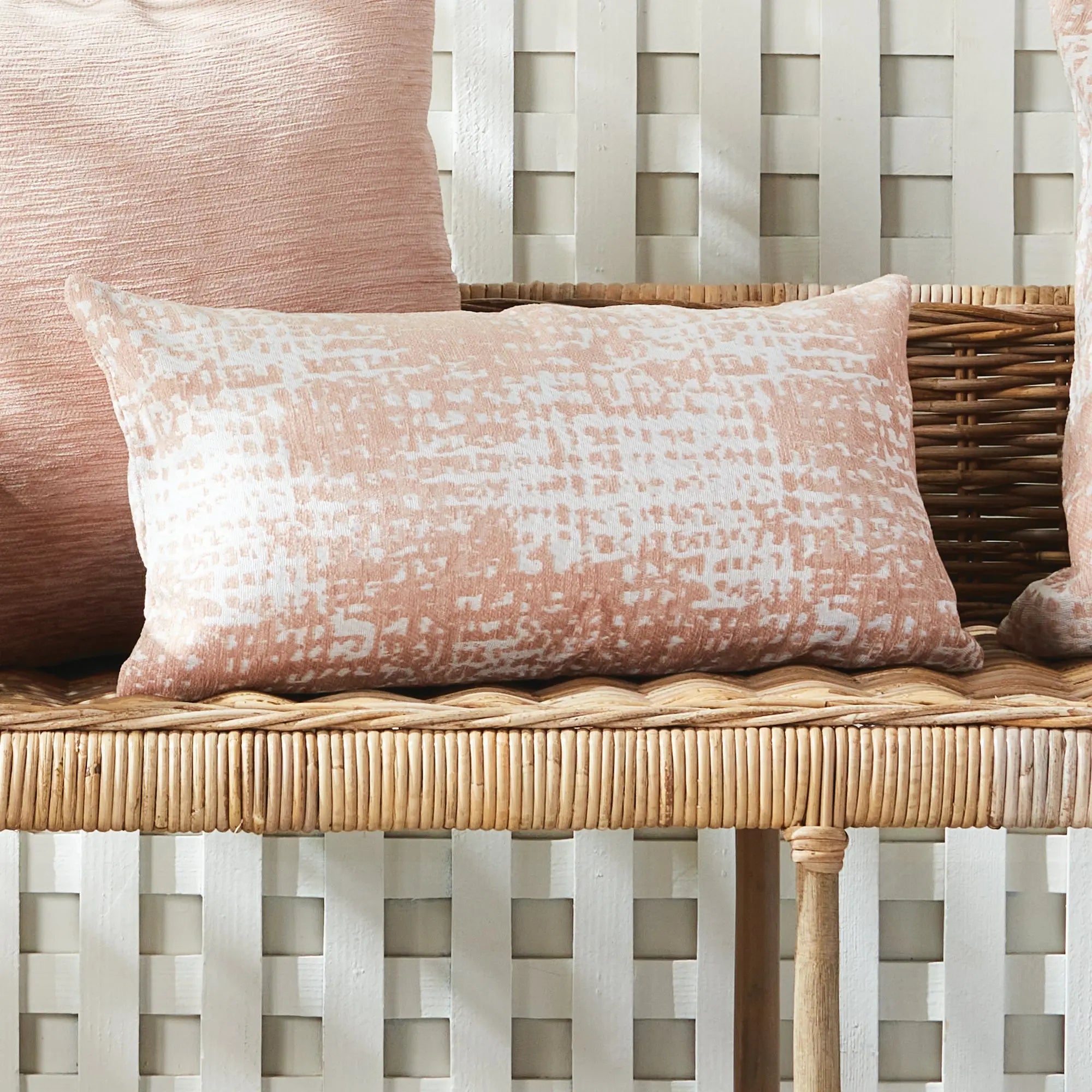Decorative pillow with a pink and white pattern on a wicker chair.