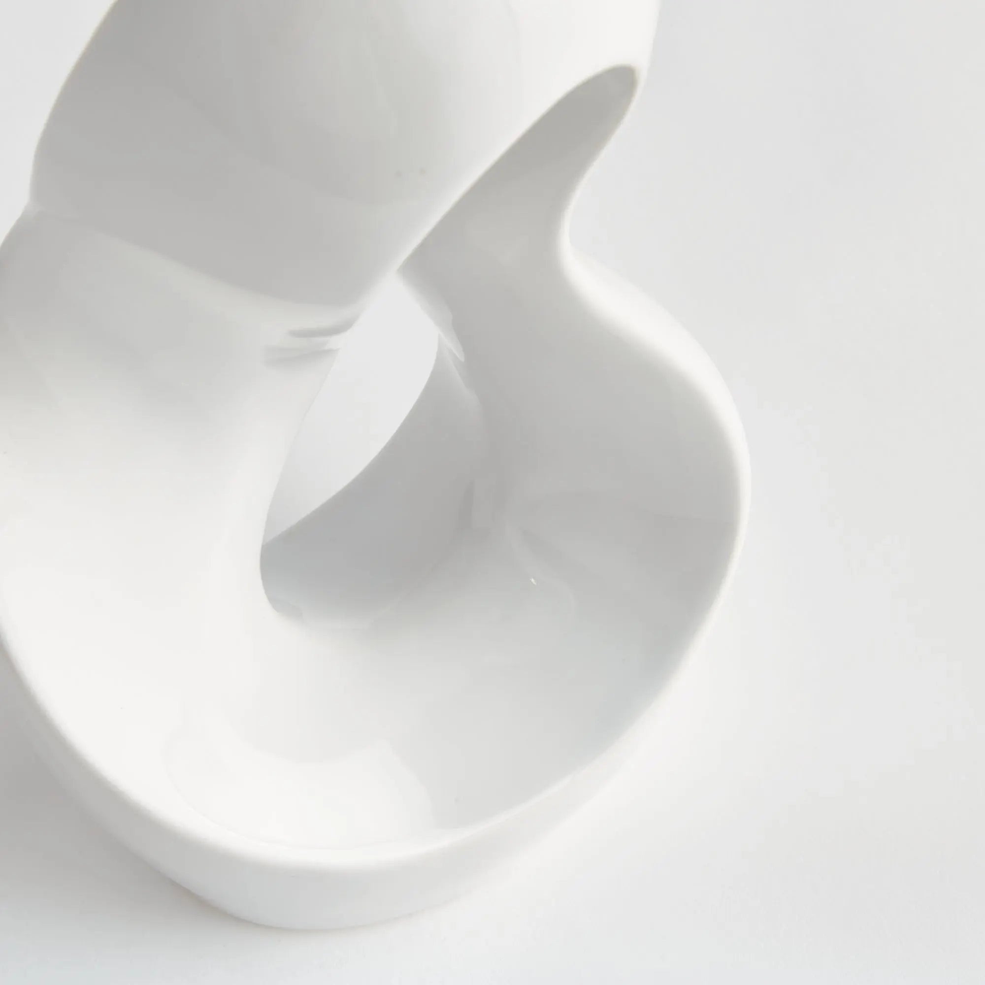 Close-up of a white ceramic sculpture with a smooth texture on a light gray background