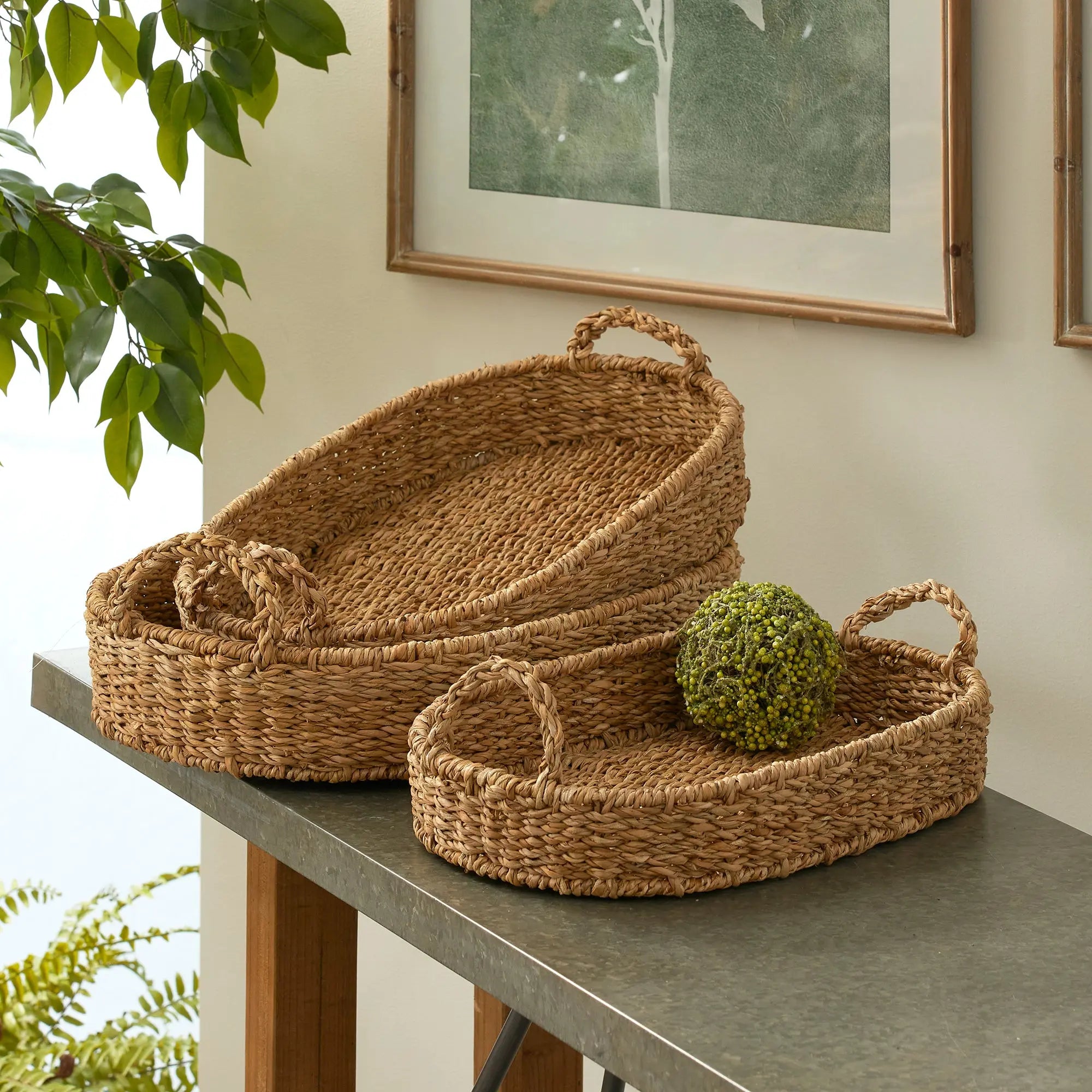Set of woven baskets on a table with a plant and framed picture in the background