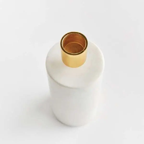 Avalyn Taper Holder, showing a modern taper candle holder with a square white marble base and a cylindrical brushed brass top. The holder is empty and is shown from a slight angle against a neutral background.