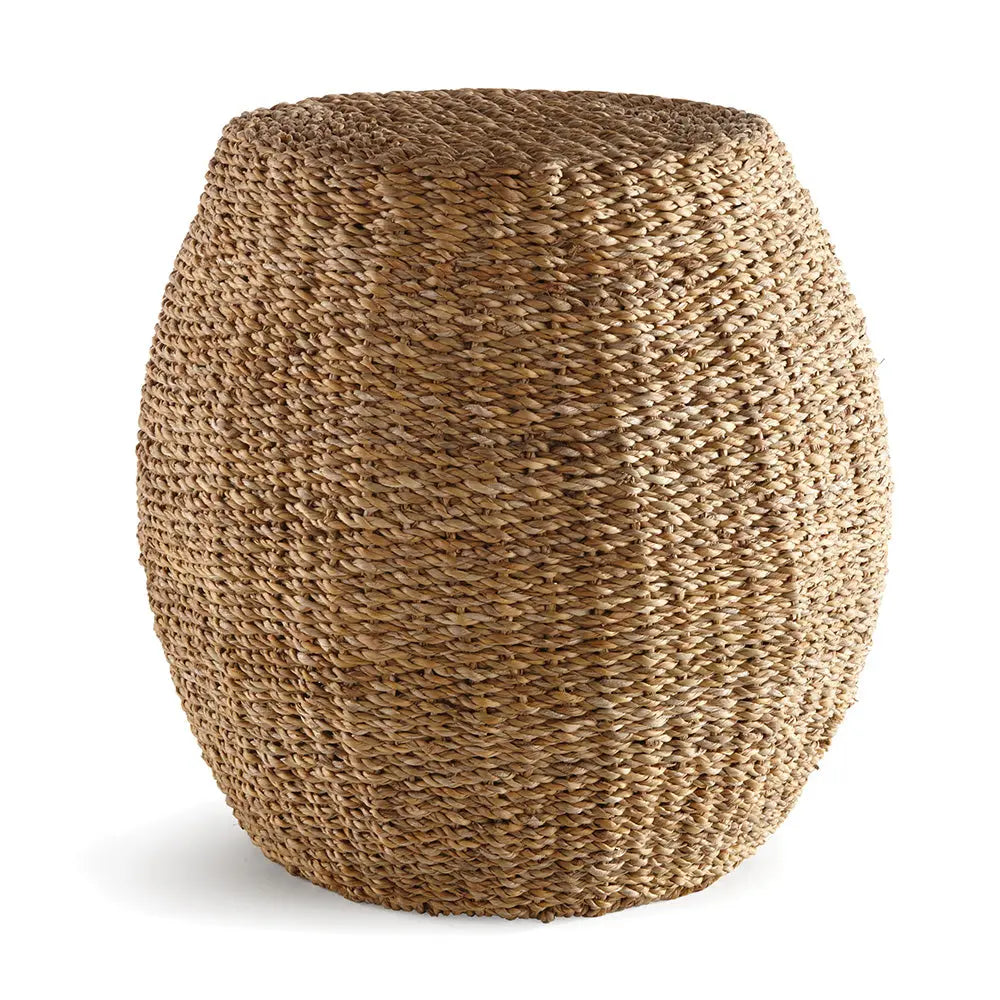 Natural seagrass hourglass pouf used as a side table with a book and coffee cup, showcasing its woven texture and versatile design.