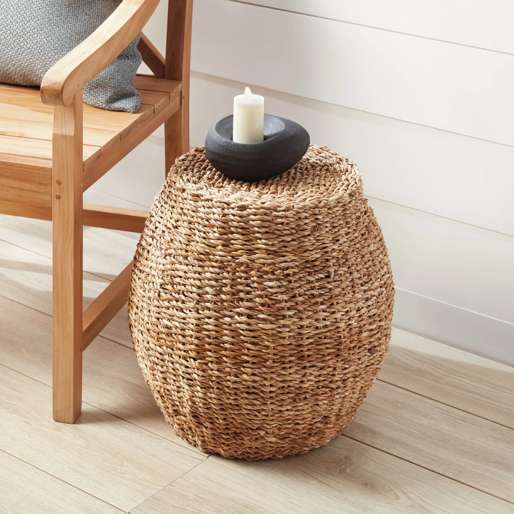 Natural seagrass hourglass pouf used as a side table with a book and coffee cup, showcasing its woven texture and versatile design.