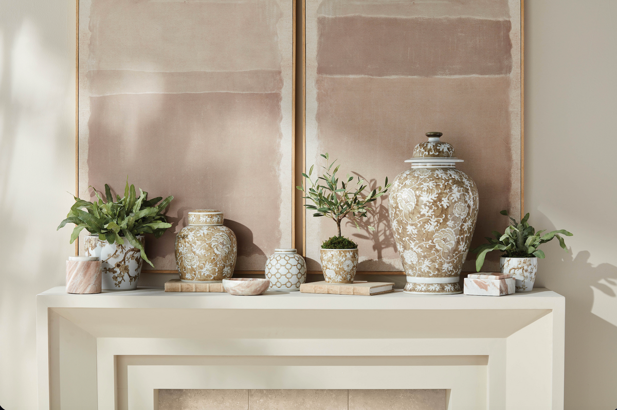 A styled interior scene showing a cream fireplace mantel decorated with multiple ceramic vases and small potted plants, set against two large beige wall panels with soft sunlight and shadows.